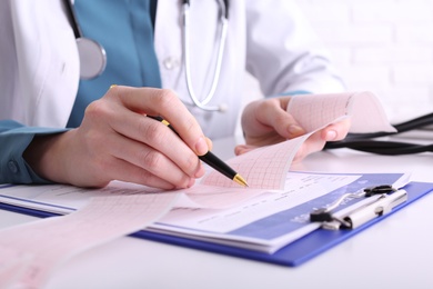 Photo of Doctor examining cardiogram at table in clinic, closeup