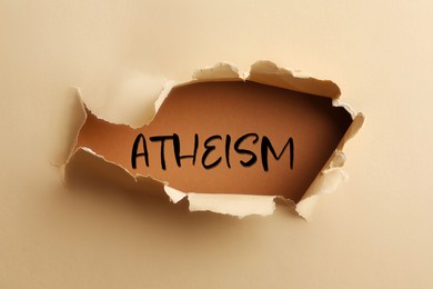 Image of Word Atheism on brown background, view through hole in beige paper