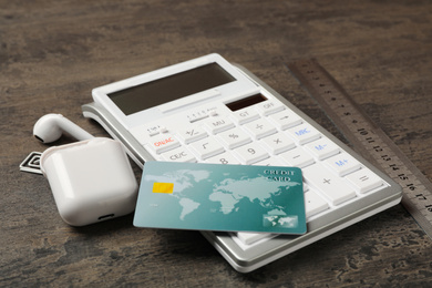 Photo of Credit card, calculator and wireless earphones on grey table