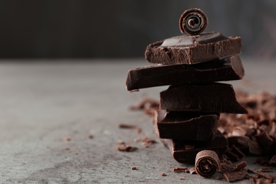 Photo of Curls and pieces of tasty chocolate on gray table. Space for text