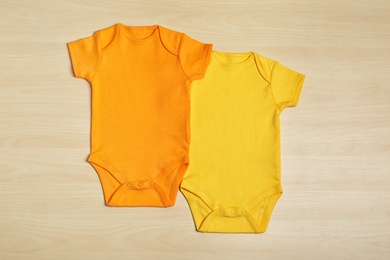 Photo of Cute baby onesies on wooden background, top view