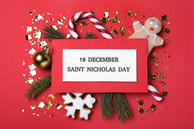 Photo of Card with text 19 December Saint Nicholas Day and festive decor on red background, flat lay