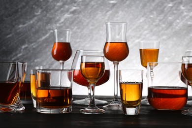 Photo of Different delicious liqueurs in glasses on dark wooden table