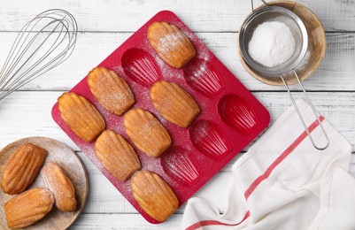 Photo of Delicious madeleine cookies and baking mold on white wooden table, flat lay