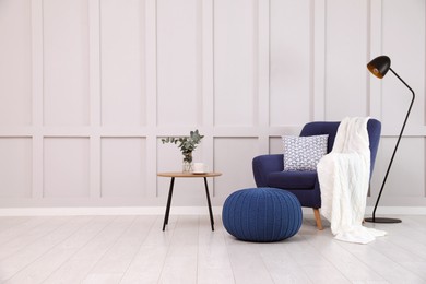 Photo of Stylish room interior with comfortable armchair and knitted pouf near white wall