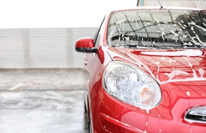 Photo of Red auto with foam at car wash. Space for text
