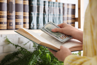 Photo of Woman hiding dollar banknotes in book indoors, closeup. Money savings