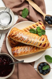Fresh tasty puff pastry with sugar powder, blueberries and mint served on white wooden table, flat lay