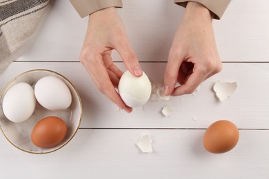 Photo of Woman peeling boiled egg at white wooden table, top view
