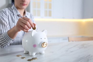 Photo of Woman putting money into piggy bank at white marble table indoors, closeup. Space for text