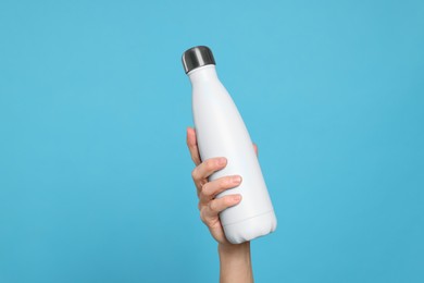 Photo of Woman holding thermo bottle of drink on light blue background, closeup
