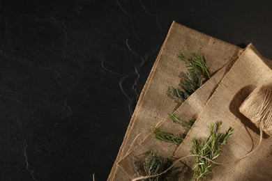 Photo of Natural burlap fabric with fresh herbs on black table, top view. Space for text