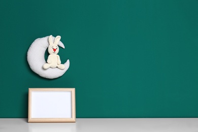 Photo of Soft toys and photo frame on table against green background, space for text. Child room interior