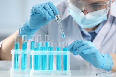 Photo of Scientist dripping liquid from pipette into test tube on blurred background, closeup