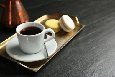 Photo of Tray with hot coffee in cup and macarons on dark textured table, closeup. Space for text