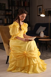 Photo of Beautiful young woman in yellow dress reading book at home