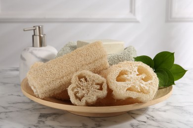 Photo of Loofah sponges, soap, towel and green leaves on white marble table