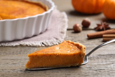 Cake server with piece of delicious pumpkin pie on wooden table, closeup