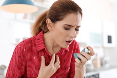 Photo of Young woman using asthma inhaler in kitchen
