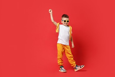 Photo of Happy little boy dancing on red background. Space for text