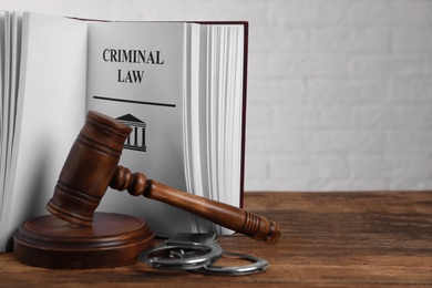 Photo of Book with words CRIMINAL LAW, handcuffs and gavel on wooden table. Space for text