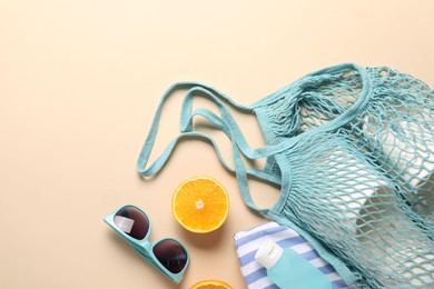 Photo of String bag, different beach accessories and orange on beige background, flat lay. Space for text