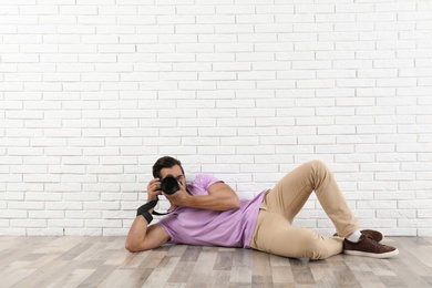 Photo of Young professional photographer taking picture near brick wall. Space for text