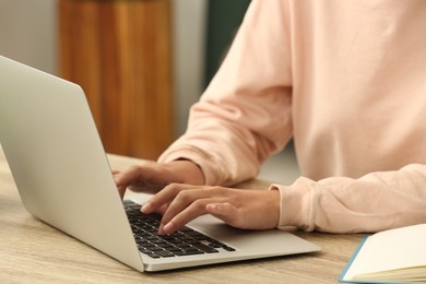Photo of African-American woman typing on laptop at wooden table indoors, closeup