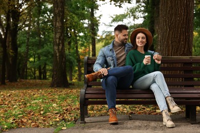 Photo of Happy young couple spending time together on wooden bench in autumn park, space for text