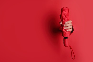 Photo of Woman holding bright umbrella through hole in red paper, closeup. Space for text