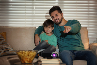 Photo of Young man and his son watching movie using video projector at home