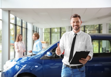 Photo of Salesman with clipboard near new car in modern auto dealership