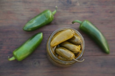Photo of Fresh and pickled green jalapeno peppers on wooden table, flat lay