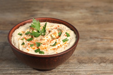 Photo of Tasty hummus with parsley and paprika in brown bowl on wooden table