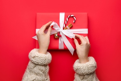 Photo of Woman holding Christmas gift box on red background, top view