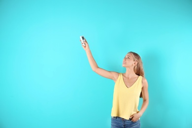 Young woman with air conditioner remote on color background, copy space text