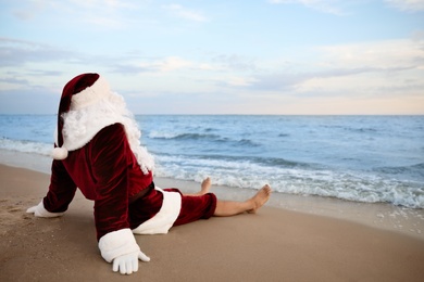 Photo of Santa Claus relaxing on beach, space for text. Christmas vacation