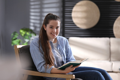 Photo of Young woman with book sitting in armchair at home
