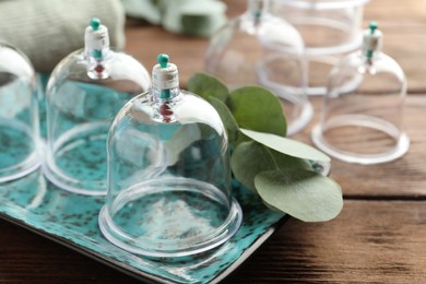 Photo of Plastic cups and eucalyptus leaves on wooden table, closeup. Cupping therapy