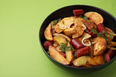 Photo of Delicious baked potato with thin dry smoked sausages, onion and dill in bowl on green table, closeup. Space for text