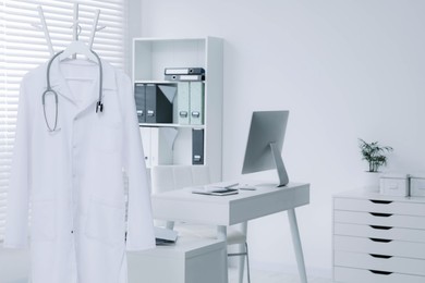 Photo of White doctor's gown and stethoscope hanging on rack in clinic