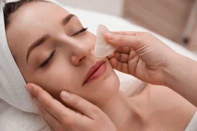 Photo of Young woman receiving facial massage with gua sha tool in beauty salon, closeup