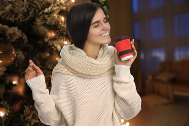 Image of Happy beautiful woman with mulled near Christmas tree indoors