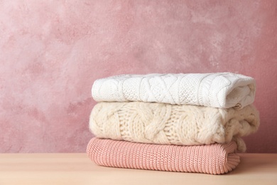 Photo of Stack of folded knitted sweaters on table. Space for text