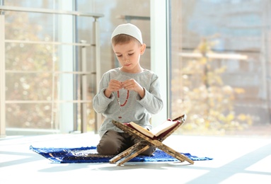 Photo of Little Muslim boy with misbaha and Koran praying on rug indoors