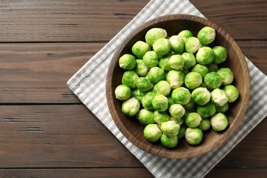 Photo of Bowl of fresh Brussels sprouts and napkin on wooden background, top view with space for text