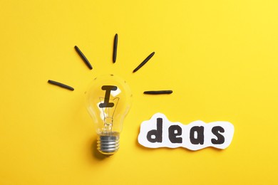 Photo of Word Ideas made with lightbulb and paper sheet on yellow background, flat lay