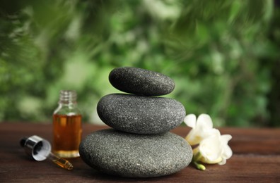 Photo of Stack of grey spa stones, oil and flower on wooden table outdoors