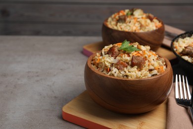 Photo of Delicious pilaf with meat and carrot in bowl on grey textured table. Space for text