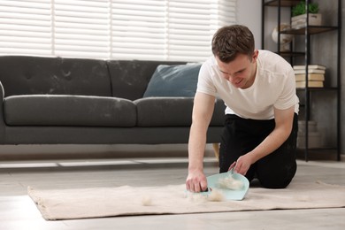 Photo of Smiling man with brush and pan removing pet hair from carpet at home. Space for text